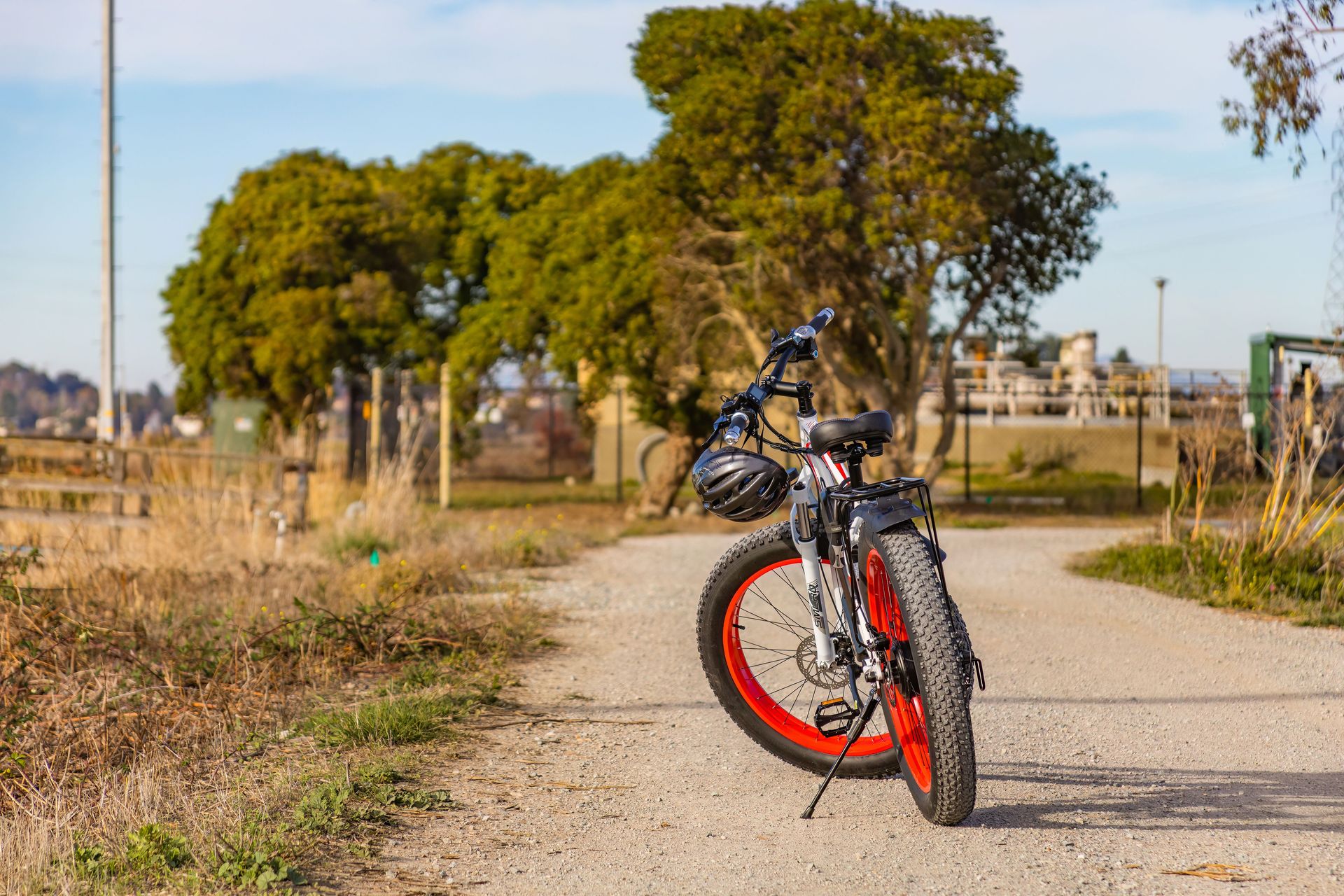 A fat tire bike with a helmet on a rural path surrounded by trees and fields.